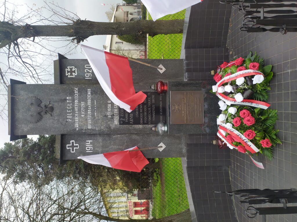 Pomnik z 1938r. udekorowany kwiatami oraz biało-czerwonymi flagami.