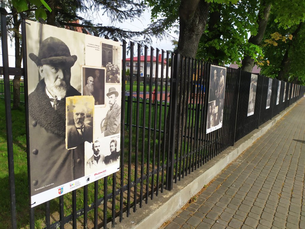 Kilka plansz wystawy ulicznej, zawieszonych na metalowym ogrodzeniu