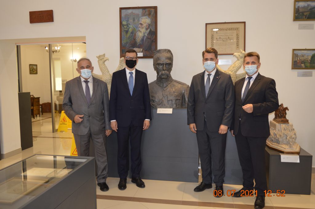 Czterech mężczyzn w garniturach, we wnętrzu muzeum. Na środku zdjęcia - popiersie Józefa Piłsudskiego.