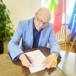 Mężczyzna w niebieskiej marynarce, podpisuje dokument