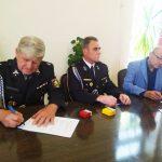 Trzej mężczyźni siedzący przy stole, w tle flaga Polski