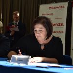 Dwie młode kobiety siedzące przy stole, jedna z nich trzyma długopis