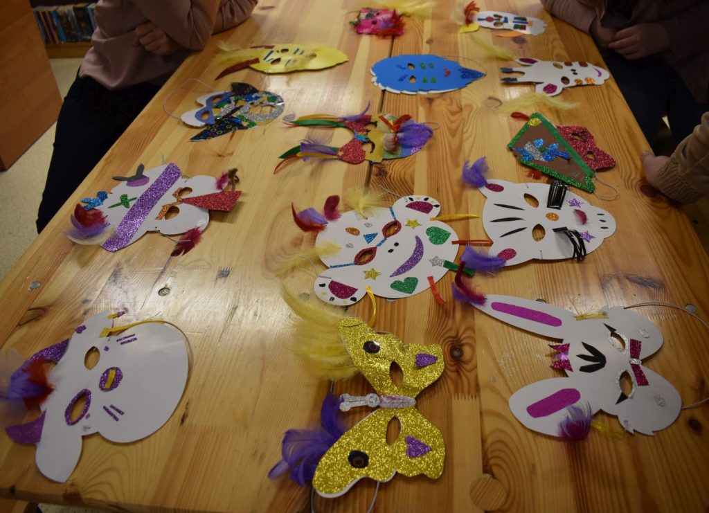 Na drewnianym stole leżą kolorowe maski karnawałowe zrobione przez dzieci