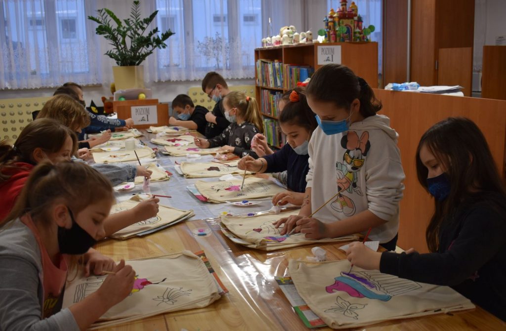 Dzieci malują kolorowe rysunki na workoplecakach w tle regały z książkami
