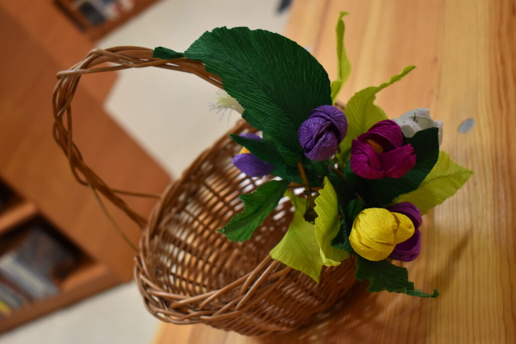 Wiklinowy koszyczek ozdobiony kolorowymi kwiatami z krepy