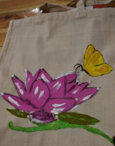 Różowy kwiat z zielonymi listkami i żółtym motylem namalowany jest na płóciennej torbie