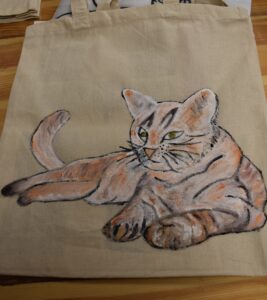 Szarobury kot w pozycji leżącej namalowany na płóciennej torbie
