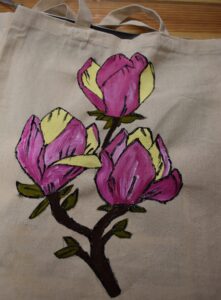Płócienna torba na której namalowana jest gałązka z trzema kwiatami magnolii w kolorze różu i żółtym