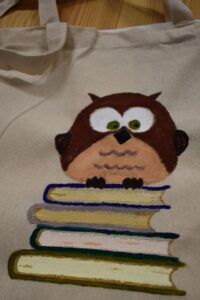 Płócienna torba z uszami na której namalowana jest brązowa sowa siedząca na czterech książkach