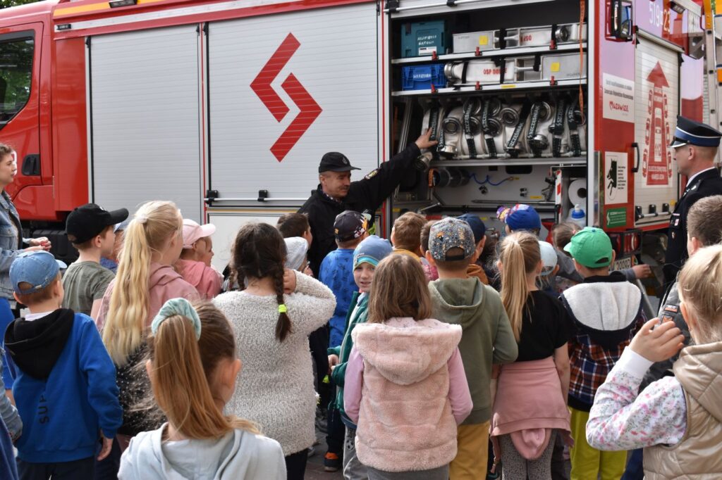 Dzieci stoją przed wozem strażackim, pan strażak opowiada im co znajduje się na wyposażeniu wozu.
