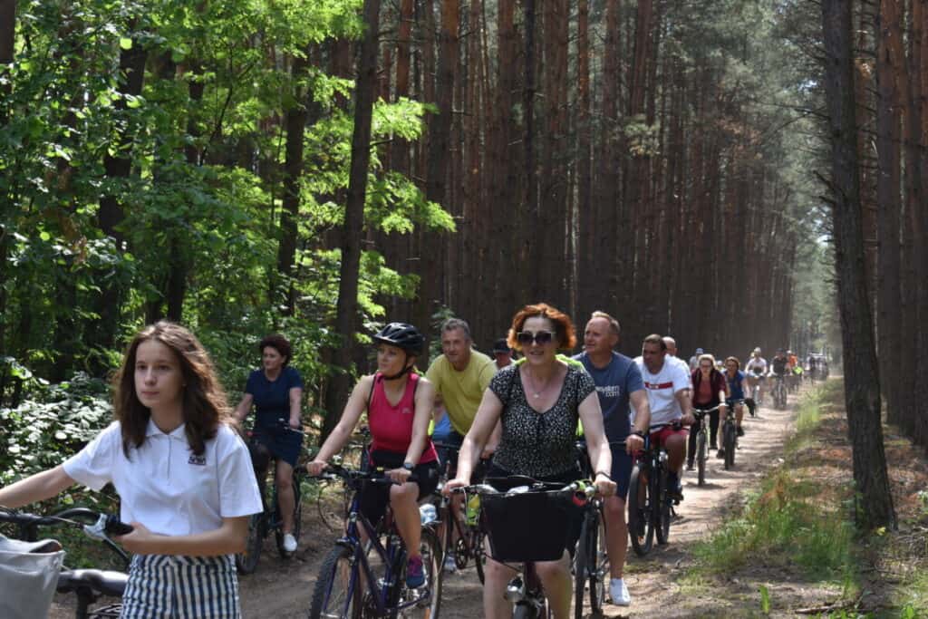 Przez las piaszczystą drogą jedzie grupa rowerzystów
