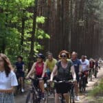 Przez las piaszczystą drogą jedzie grupa rowerzystów