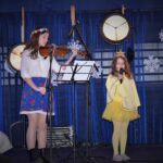 Dziewczynka grająca na skrzpcach. Dziewczynka trzymająca mikrofon.