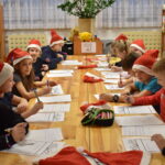 Dzieci siedzące przy drewnianym stole w czerwonych czapkach