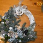 422 Biały pleciony wianek z dużą ilością gałązek świerku, złotymi bombkami i kokardą.