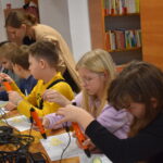 Na zielonym dywanie siedzą dzieci w kółku.