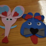 187 W bibliotece przy drewnianym długim stole siedzą dzieci i rysują na szklankach wzory. W tle regały z książkami,