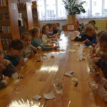 Trzy dziewczynki siedzą przy stole i rysują pomarańczowymi długopisami 3D