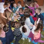 Kobieta trzyma kuferek w ręku i pokazuje go dzieciom, one go dotykają.