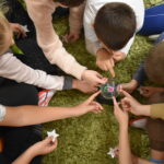 Na zielonym dywanie stoi kula a dzieci siedzące w kole dotykają ją rękoma