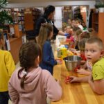 Dzieci w Bibliotece na drewnianym stole zabierają się do pieczenia pierników. W tle regały z książkami