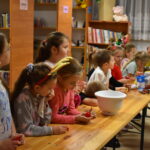Dzieci w Bibliotece na drewnianym stole zabierają się do pieczenia pierników. W tle regały z książkami