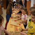 Dzieci w Bibliotece na drewnianym stole zabierają się do pieczenia pierników. W tle regały z książkami