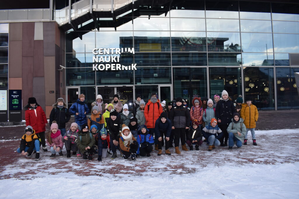 80 Na tle szklanego budynku z napisem Centrum Nauki Kopernik grupa dzieci ubrana w ciepłe kurtki na chodniku przed nimi leży śnieg
