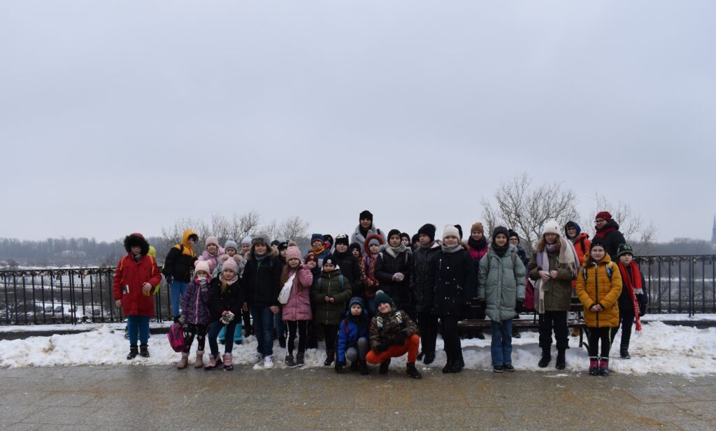 139 Grupa dzieci stoi a dwóch chłopców kuca. W tle zimowy krajobraz Warszawy