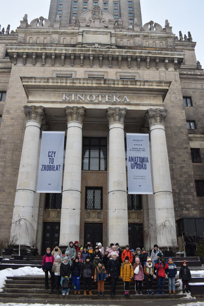 169 Grupka dzieci stoi na schodach na których leży śnieg, w tle budynek Pałacu Kultury i Nauki w Warszawie