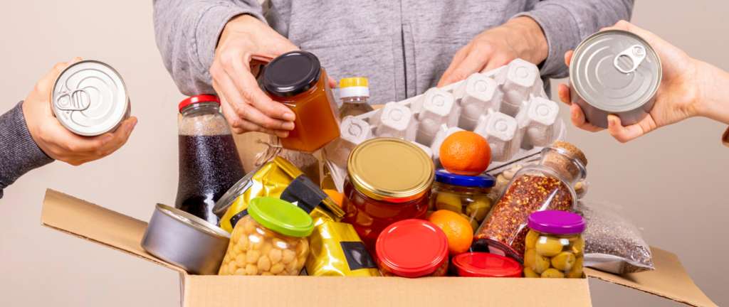 Na obrazku grupy ludzi, którzy wkładają jedzenie do kartonowego. Udostępnia, że angażuje się w działania charytatywne lub przygotowuje paczkę na zbiórkę żywności.