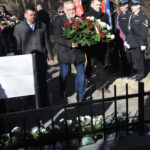 DSC_0295 Na obrazku widać grupę osób stojących przed ogrodzeniem. Wyglądają na podejrzane lub skupione, podejrzanec, że może wykryć coś poza klastką.