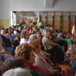 Na udostępnienie jest grupa ludzi siedzących w pomieszczeniu. Wydają się być skupieni, co może sugerować spotkanie, seminarium lub inną formę zbiorowego zgromadzenia.