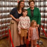 Na obrazku trzy kobiety i dziecko na czerwonym dywanie. Wszyscy są elegancko ubrani, co do zasady, że mogą brać udział w prestiżowych wydarzeniach lub galii.