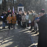 DSC_07351 Na obrazku widać grupę osób, która stoi gdzieś obok pomnika, otoczonego z każdej strony lasem. Dominuje bujna zieleń duże drzewa oraz występy pośrodku scen jest centralnym widokiem.