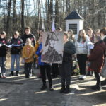 DSC_0765 Grupa ludzi stoi w leśnej okolicy, otoczeni drzewami o różnych gatunkach i rozmiarach. Jedni z nimi rozmawiają ze sobą, inni podziwiają piękno natury i cieszą się spokojem leśnej scenerii.