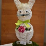 Na obrazku widnieje dekoracyjna rzeźba królika z muszką i okularami, która jest wystawiona na drewnianym pniu. Królik ma elegancki wygląd dzięki dodatkom, które ma na siebie.