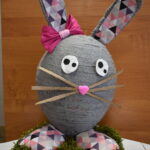 Na obrazku dekoracyjnym wielkiego królika, wykonanego z szarego i różowego materiału, który jest wystawiony na pościel z sztucznych trawy. Królik ma sympatyczną minę i brzmi na delikatnym w dotyku.