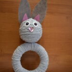 Na karcie jest robione rzemiosło kota, wykonane z zestawu owiniętego szarego włóczkiem, do którego zostały utworzone papierowe uszy i narzędzia. Tło zapewnij drewniane deski.