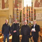 Na obrazku czterech mężczyzn stojących w kościele. W tle zaznaczamy dekoracje w postaci kolorowych wstążek.