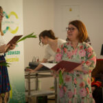 Na zdjęciu kobieta ubrana w kwiecistości. Wygląda elegancko i stylowo, a całość jest urocza, podkreślając delikatne światło padające na tło.