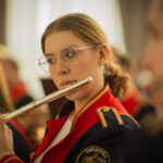 Na obrazku kobiety grającej na flecie. Ona jest skupiona, a w tle można uzyskać niewyraźne kontury otoczenia.