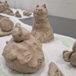 438888106_465346015840925_7346507683375529773_n Na obrazku są gliniane figurki zwierząt, które występują na białym tle. Zwróć uwagę na siedzącą figurę kota, a zaraz przed nią pojawi się mały, zaokrąglony model.