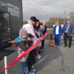 Na obrazku grupy ludzi, w tym dzieciach, biorących udział w ceremonii przecinania wstęgi przed żywym dostępem. Budynek ten nazywa się „świetlica Wólka Kokosia”.