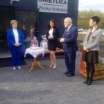 Na zdjęciu są cztery osoby dorosłe, dwóch mężczyzn i dwie kobiety, które są dostępne przed wejściem z napisem „świetlica wółka kokosia”. Obok nich widoczny jest stół z koszykiem oraz biały koronkowy obrusem.