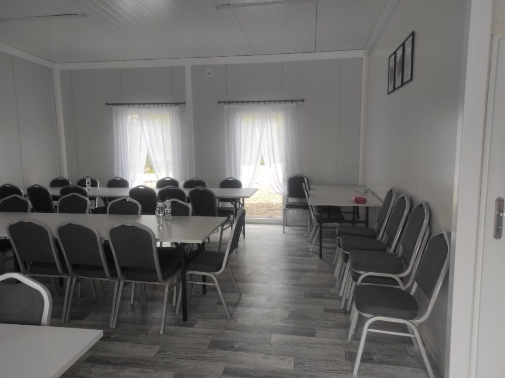 Na obrazku widocznym pustą klasę z rzędami stolików i krzeseł, białe zasłony na oknach oraz szare podłogi. Po prawej stronie można umieścić dwie ramki zamocowane na ścianie.