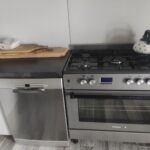 Na obrazku głównym, który dominuje przed zagrożeniem, następuje pierwsze w zmywarce. Na blacie znajduje się drewniana deska do krojenia, obok znajduje się płyta gazowa kuchenna, której stoi czajnik.