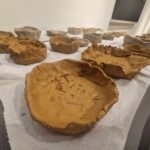 Na obrazku są gliniane miski w różnych fazach suszenia, rozłożone na papierowych ręcznikach na stole. urządzenie z misek ma surowy, aplikacyjny formowany wygląd, podkreślający rzemieślniczy charakter.