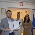 Na obrazku znajdują się trzy osoby - dwie kobiety i jeden mężczyzna, którzy są objęci certyfikatem. W tle widoczne są godło Polski i flagi Unii Europejskiej.