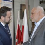 Na zdjęciach dwóch mężczyzn ubranych w ubrania biznesowe, którzy rozmawiali ze sobą podczas wydarzeń w pomieszczeniu. W tle znajdują się flagi i historyczne artefakty.